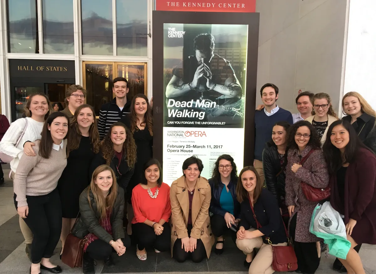 A group poses inside the Kennedy Center beside a poster for the Washington National Opera production Dead Man Walking.