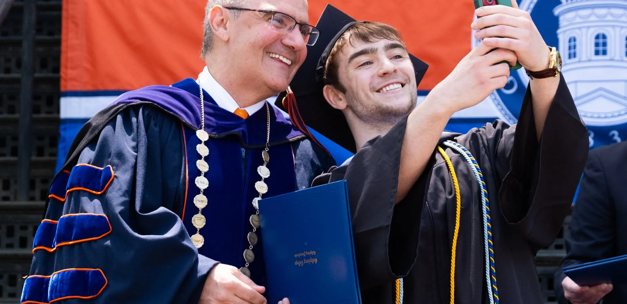 Student takes selfie in regalia at Commencement with President Iuliano