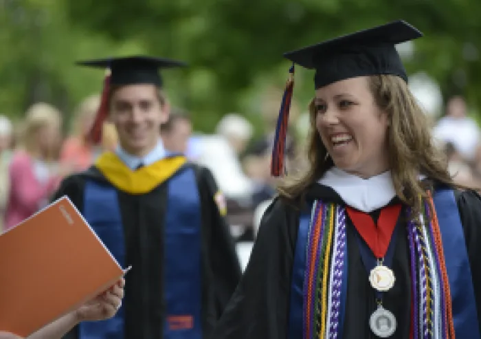 Smiling graduate wearing medals and colorful cords during commencement.