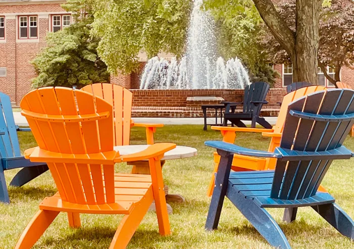Colorful Adirondack chairs surround a table near a campus fountain.