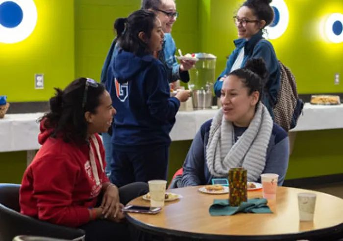 The group of students chat around a table.