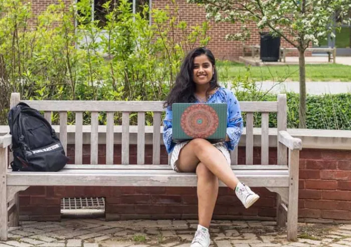 A student works on her laptop while sitting on a bench.