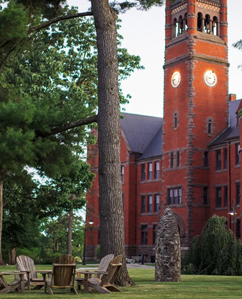 Evening view of Glatfelter Hall’s red‑brick clock tower behind trees and lawn chairs.