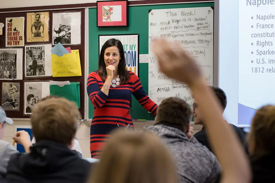 speaker smiles at classroom with student hand raised in foreground
