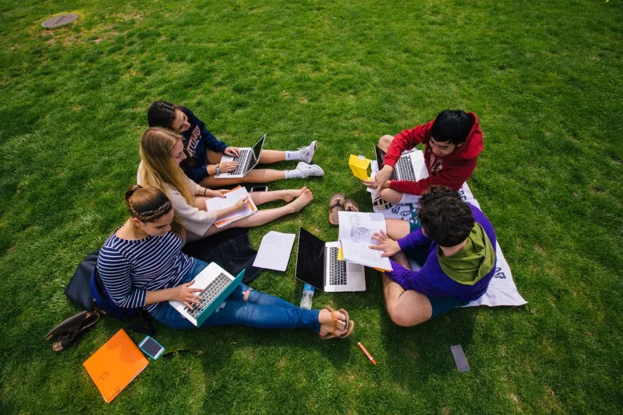 photo of students from above seated together with books and laptops on lawn