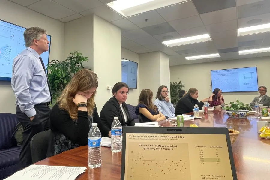 students sit at business table with election analytics on screens in foreground and background