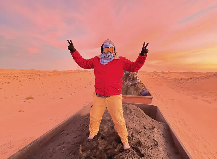 gloved and masked student in goggles poses on train in desert