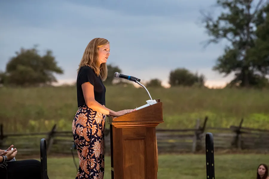 female prof speaks at podium with Gettysburg battlefields in background
