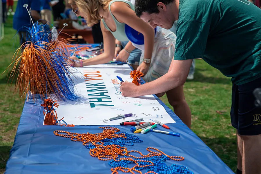 students sign big thank you banner on table outside