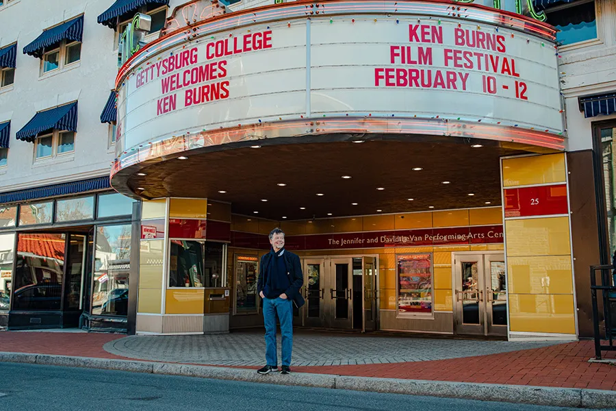 Ken Burns poses on sidewalk in front of Majestic Theater beneath marquee with his name