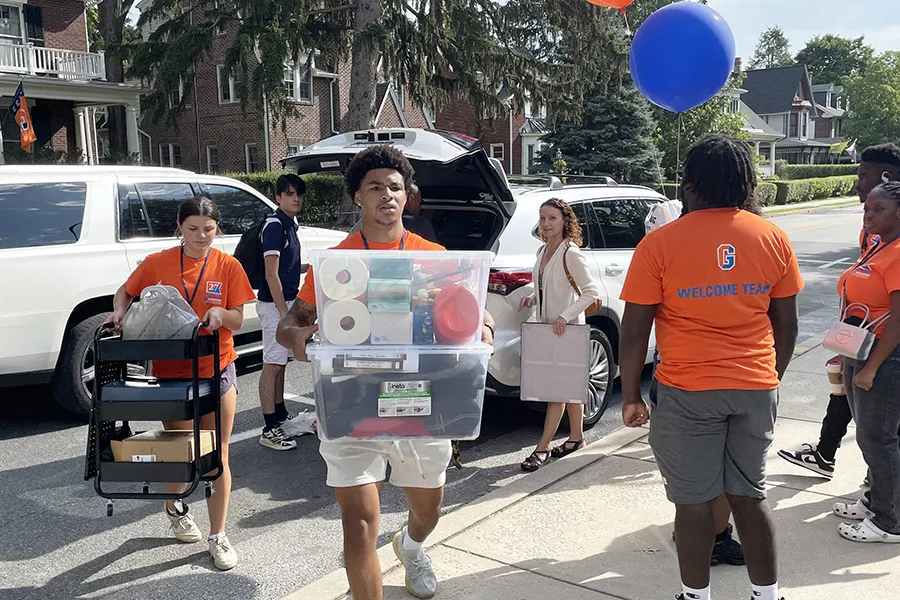student welcome team members carry new first year's belongings in from white car