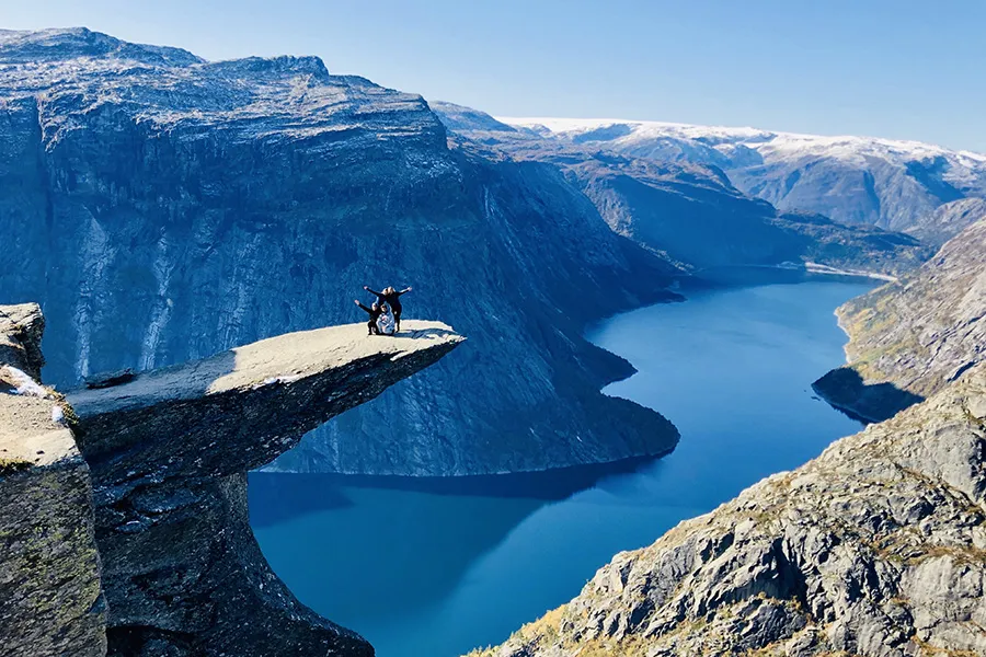 group of students pose with arms in air on cliff in front of majestic fjord