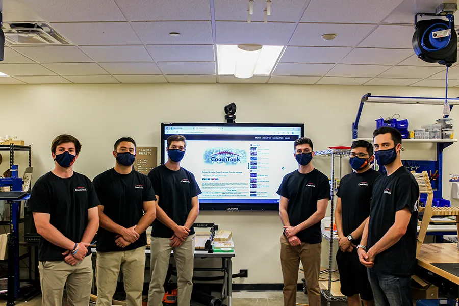 masked male students stand in front of "CoachTools" on digital display