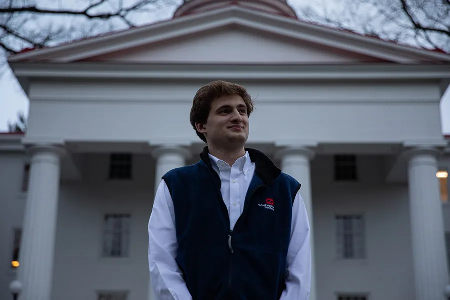 male alum standing in front of building with pillars