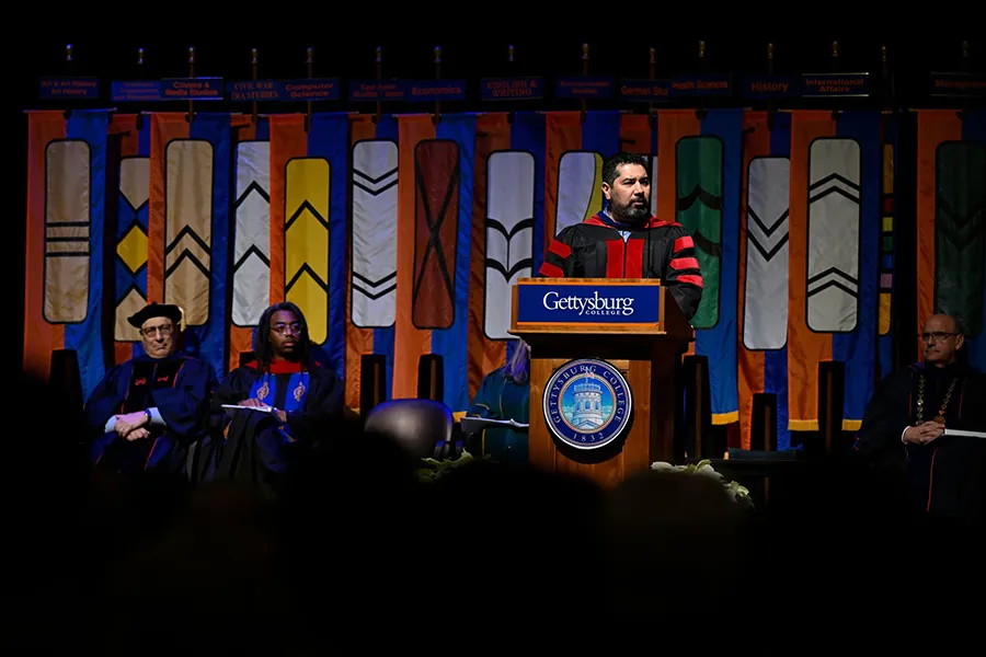 professor speaks at podium in front of major commencement banners
