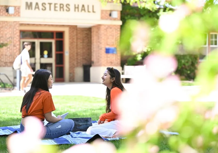 female students sit on blanket on grass outside Masters Hall