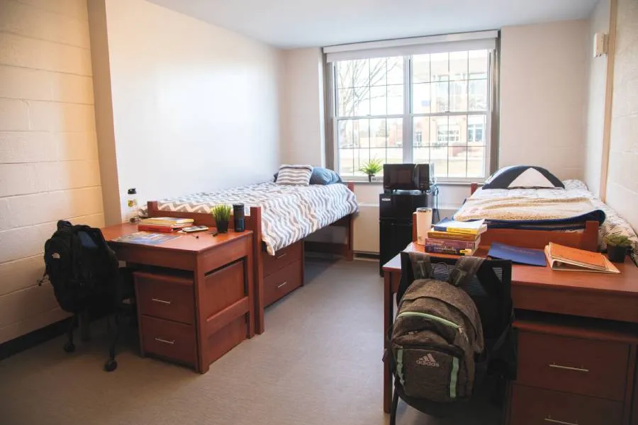 dorm room with student supplies on desks and made beds