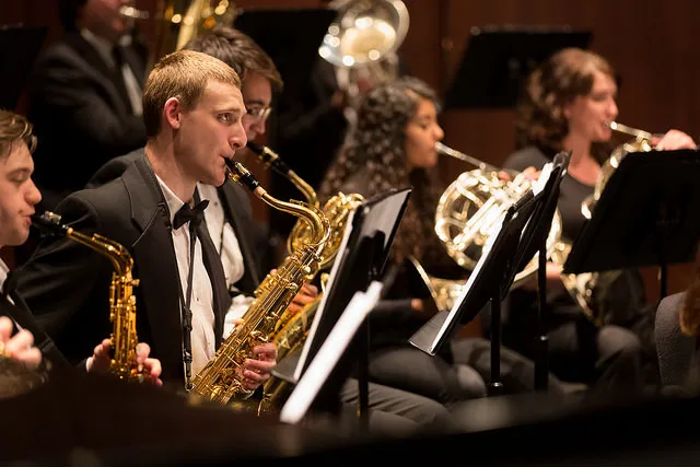 Student musicians perform saxophones and French horns in an ensemble.