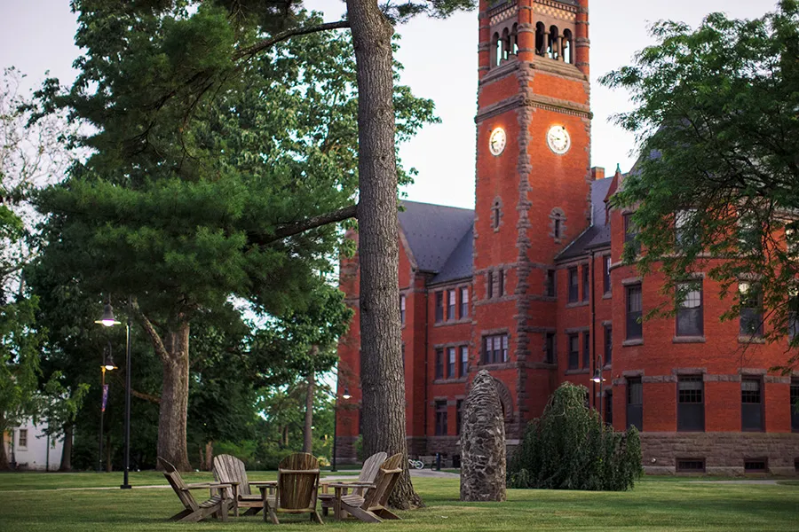 Evening view of Glatfelter Hall’s red‑brick clock tower behind trees and lawn chairs.