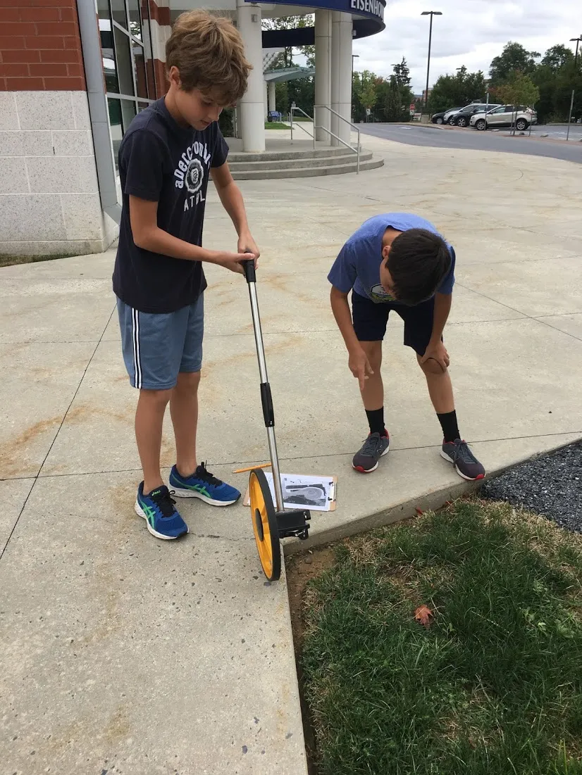 Two students using tools to work on a landscaping project outside.