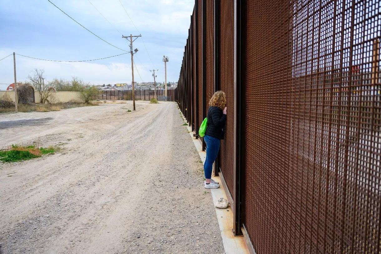 A student looks through the fence at the U.S.-Mexico border.