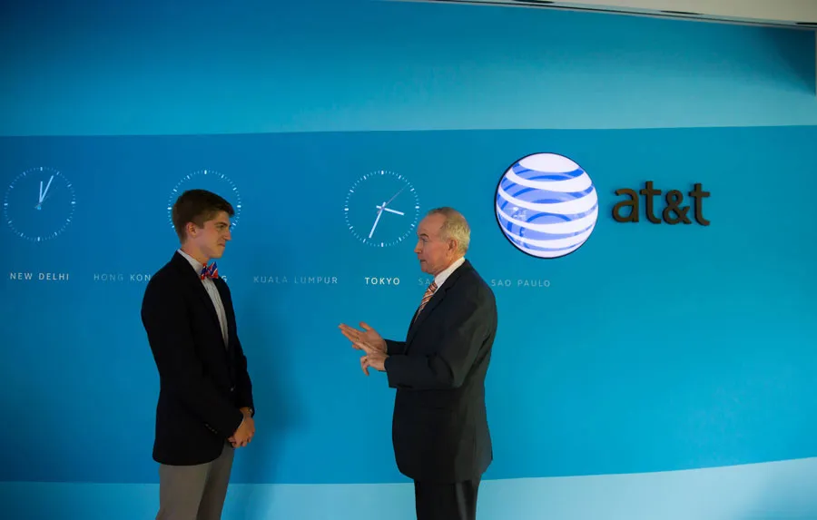 Two men converse in front of an AT&T world-clocks display.