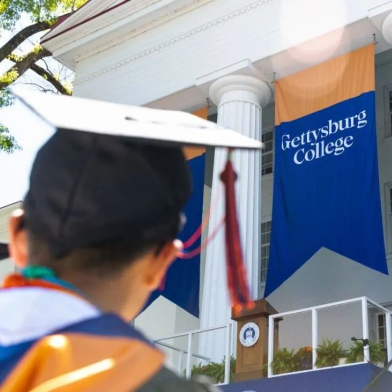 Graduate in cap and gown walks past a campus sign.