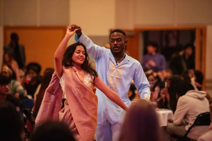 Two students perform together at an indoor cultural event while an audience watches