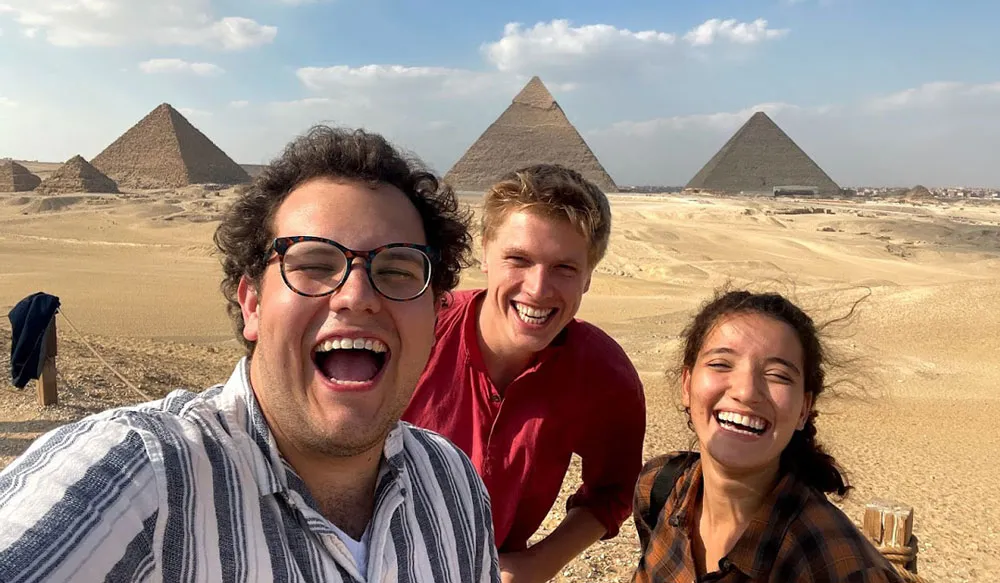Three students take a selfie in front of the pyramids at Giza.