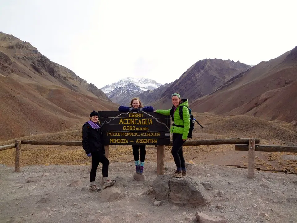 students pose by sign in front of mountain