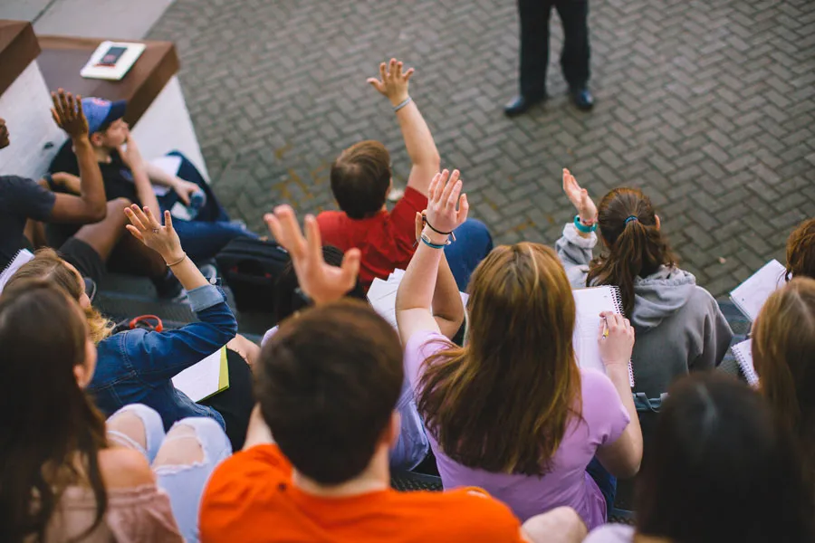 Students in a classroom raise their hands.