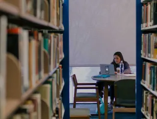 Student studying in a library aisle.