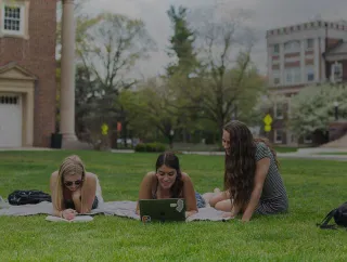 Three students working while they lie on the grass.