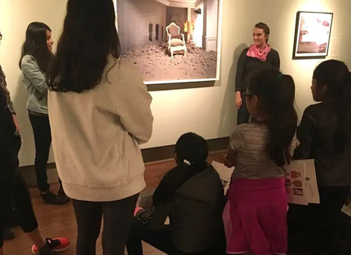 A student gallery attendant explains a painting to an audience.