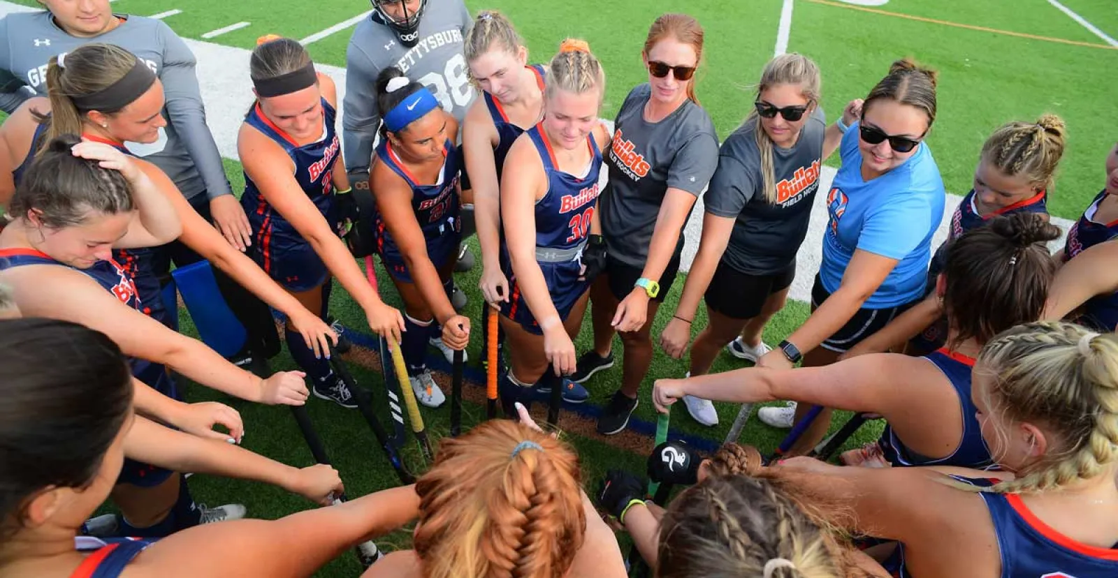 Field hockey team members putting their hands together in the middle of a circle