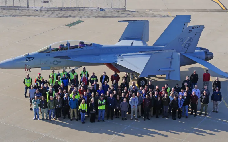 large group of people pose on ground in front of parked fighter jet