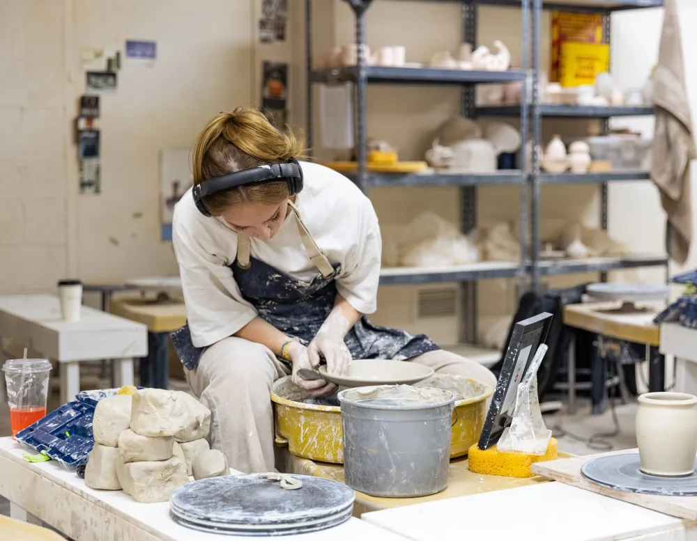 student throws pottery on wheel in ceramics studio
